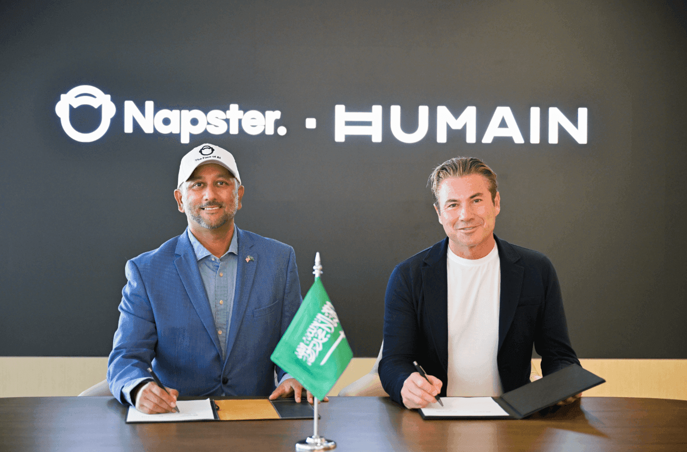 Two representatives signing documents in front of Napster and HUMAIN branding.