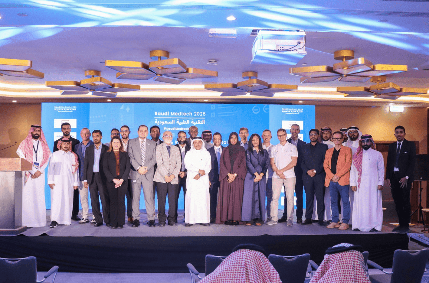 Group of conference attendees posing together on a lit stage.