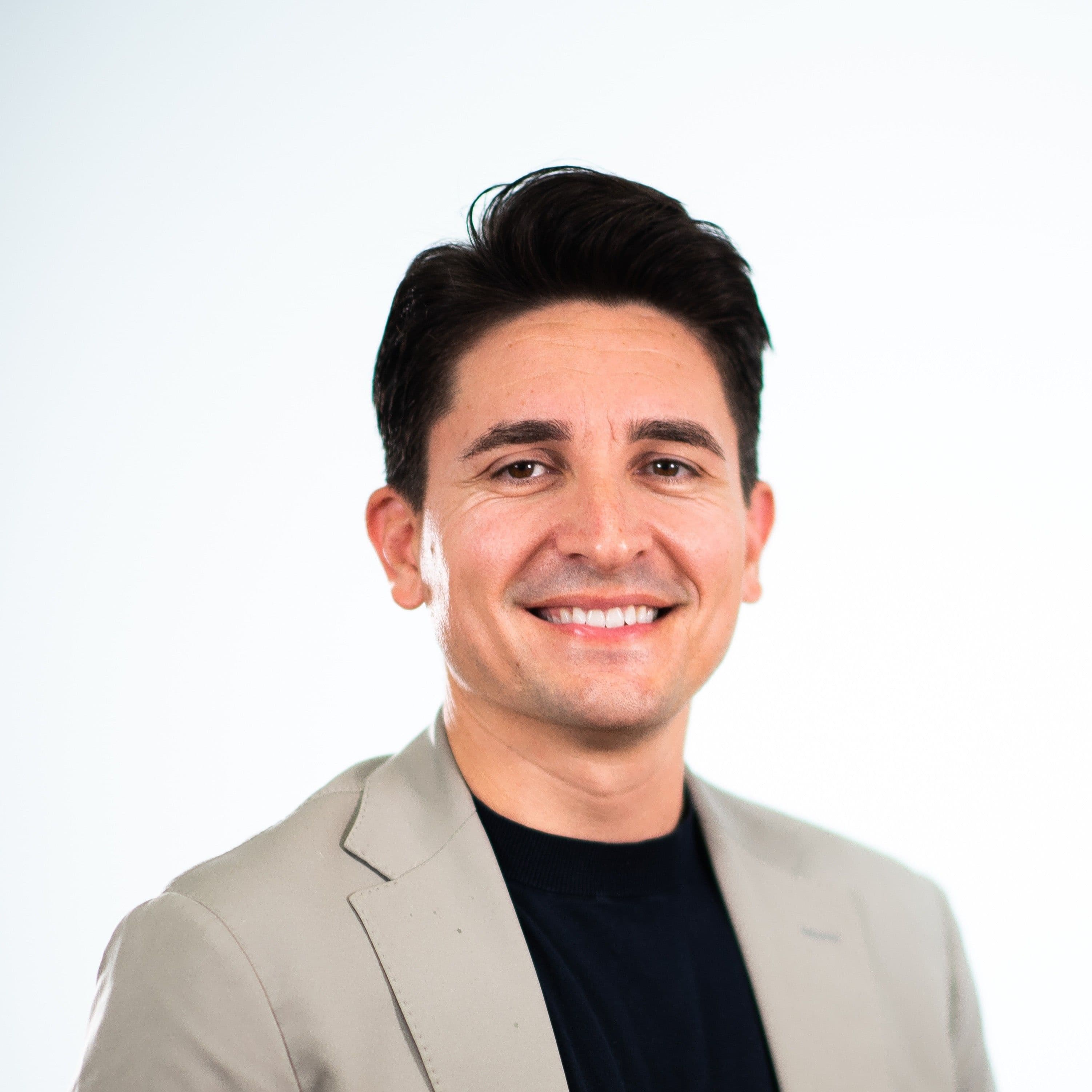 Portrait of a smiling man wearing a light-colored jacket over a black shirt.