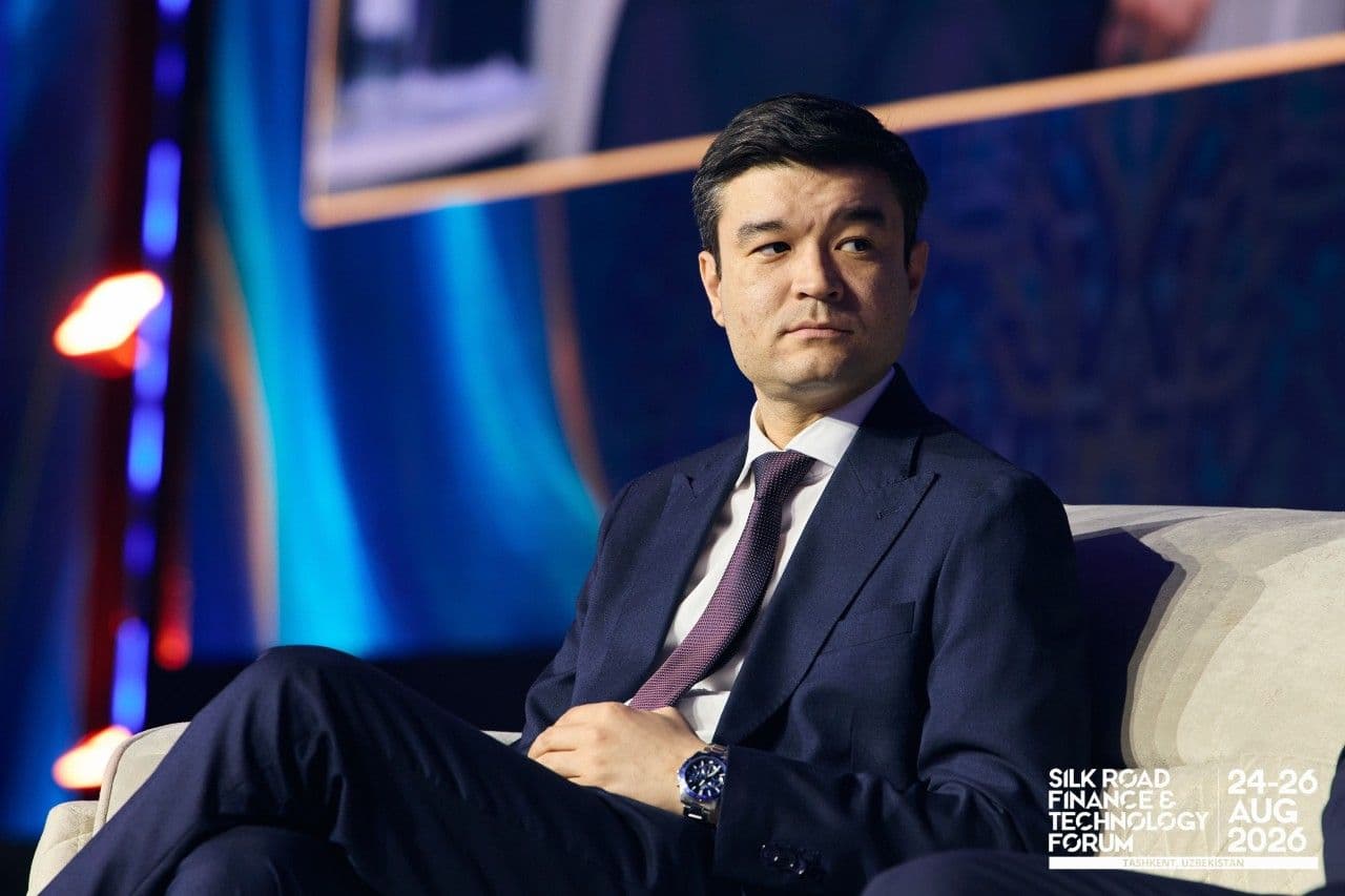 Man in a dark suit seated on a conference stage.