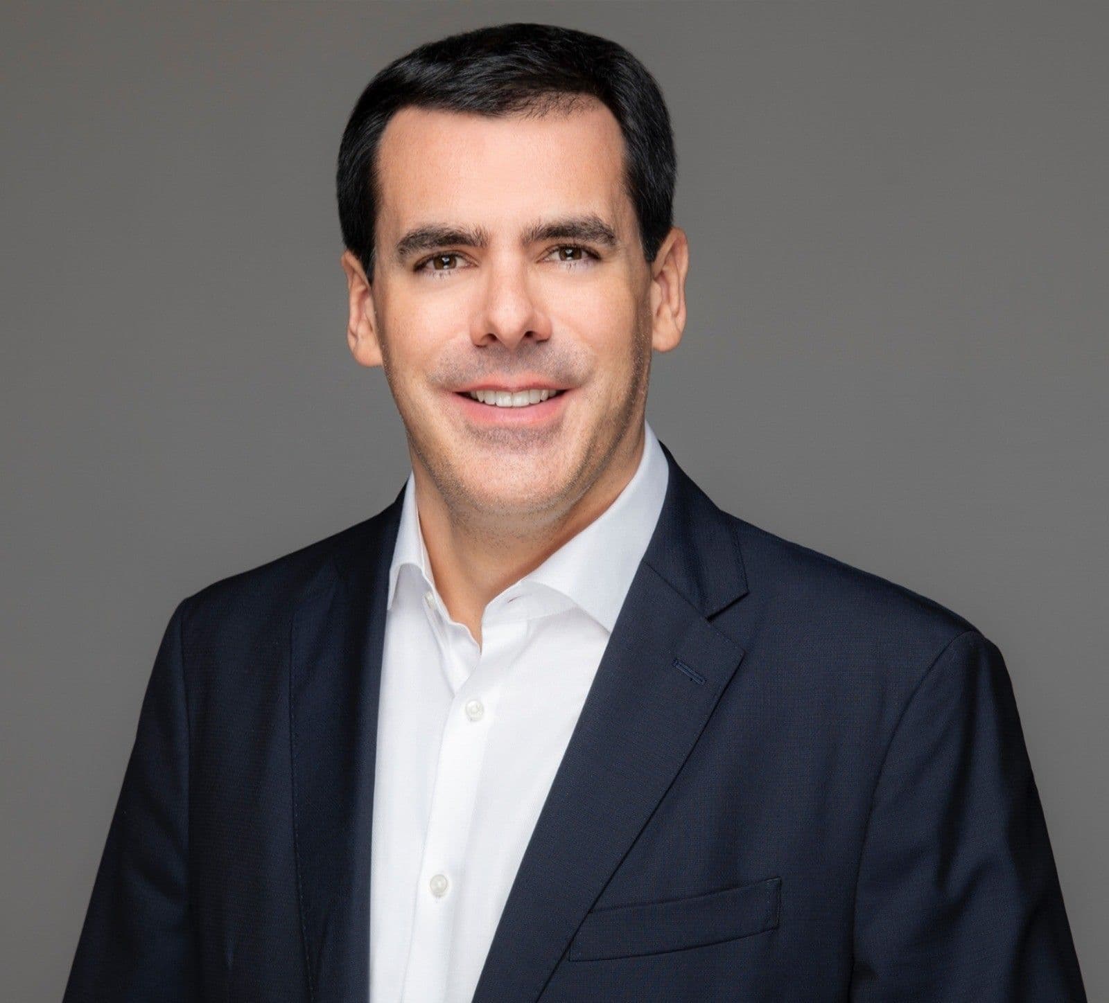 Portrait of a smiling man wearing a dark jacket over a white shirt.