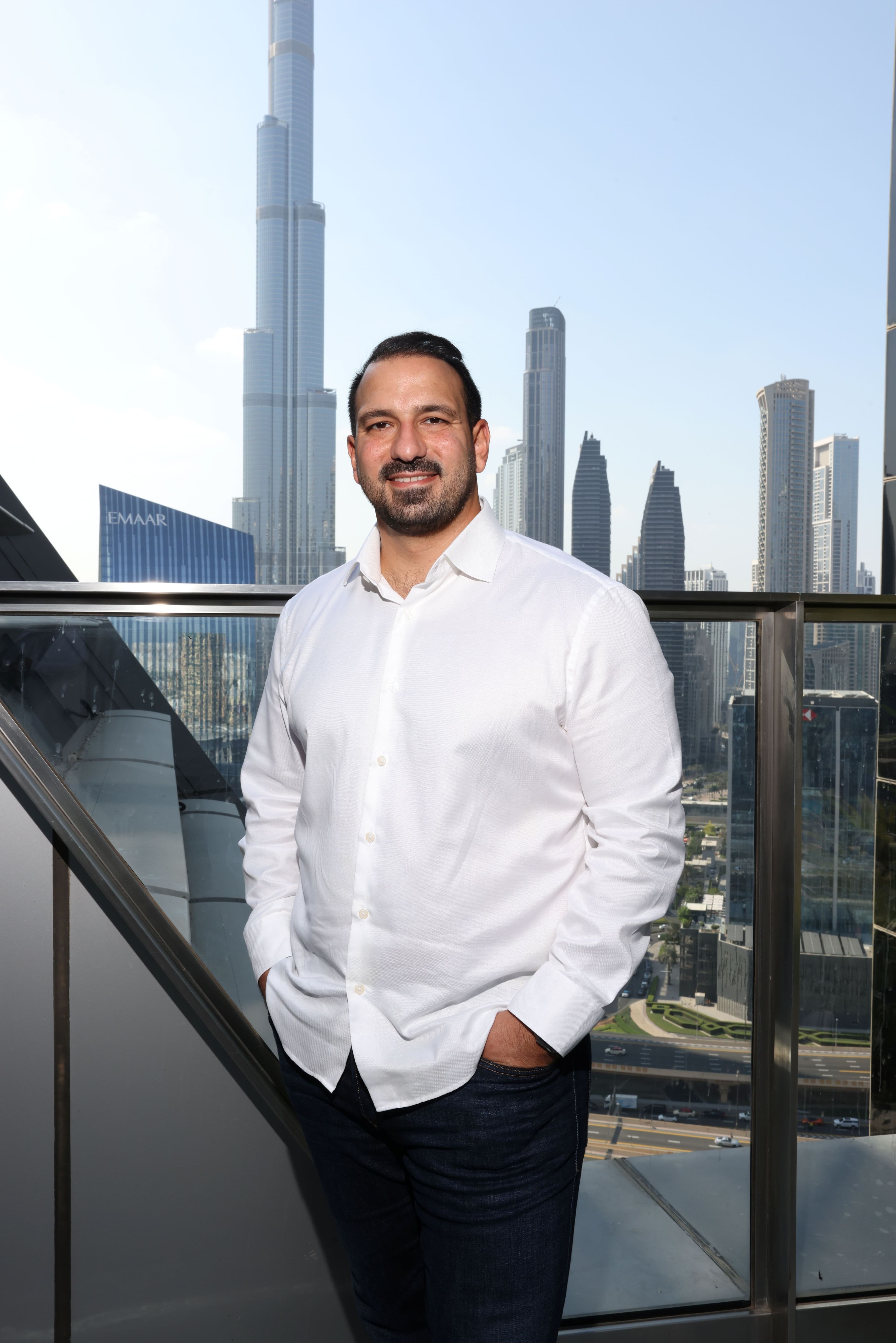 Portrait of a man in a white shirt beside office windows.