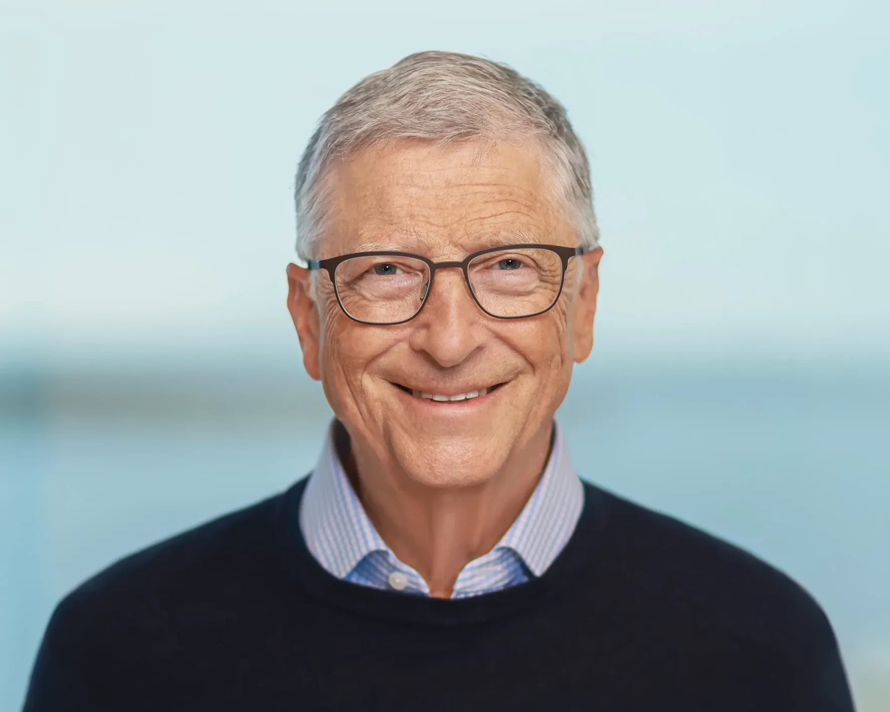 Portrait of a smiling man wearing glasses and a dark sweater over a collared shirt.