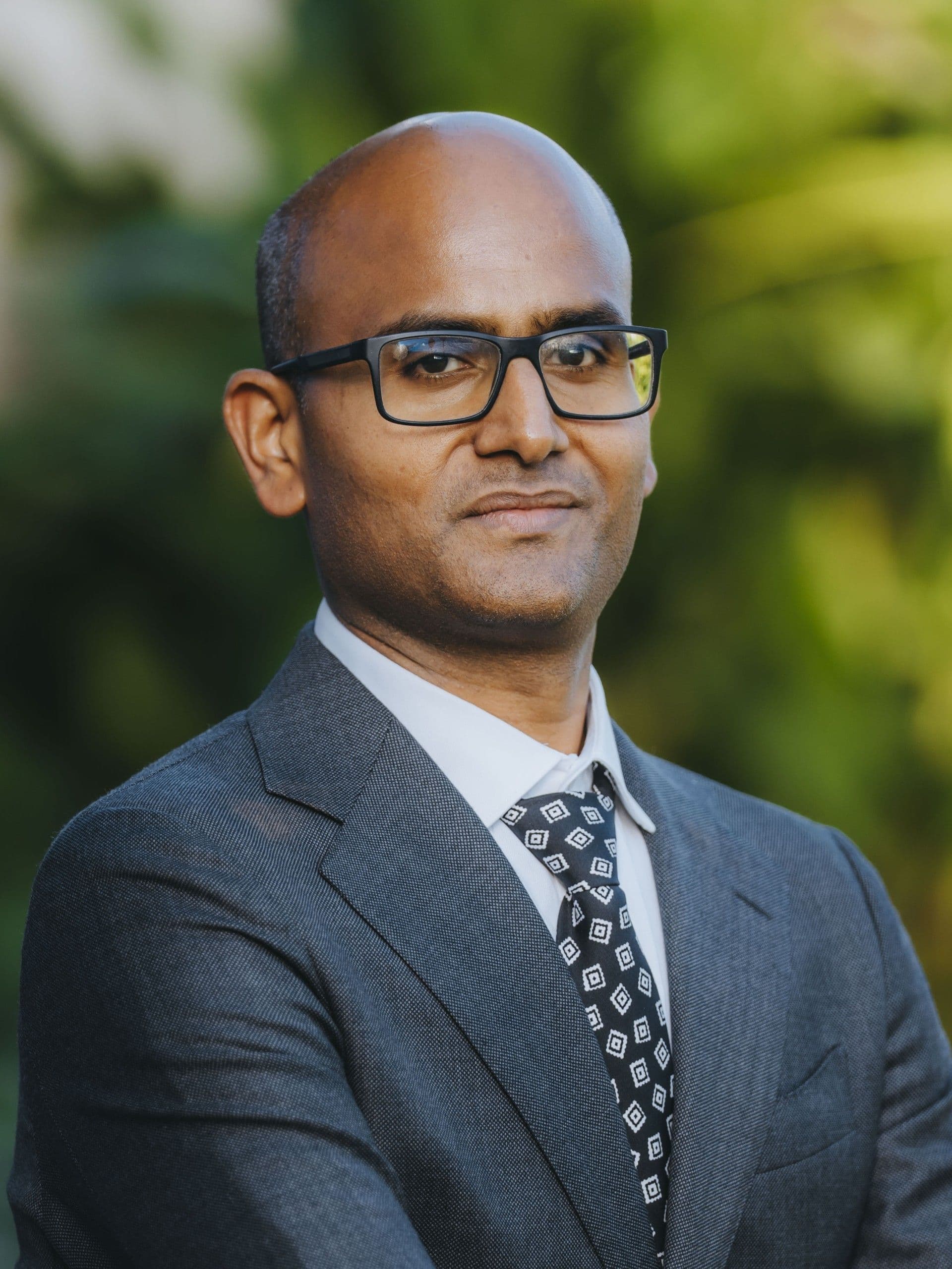 Portrait of a man wearing glasses, a dark suit, and a patterned tie.