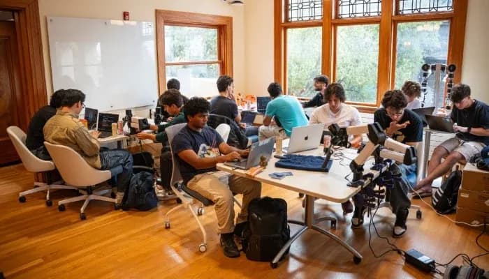 Students working together on laptops around a table in a bright room.