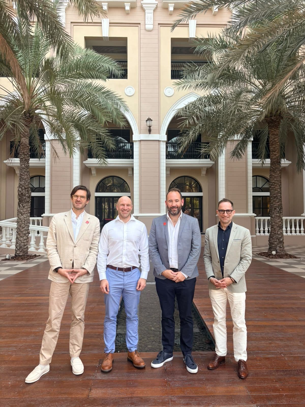 Four men standing together in a palm-lined courtyard.