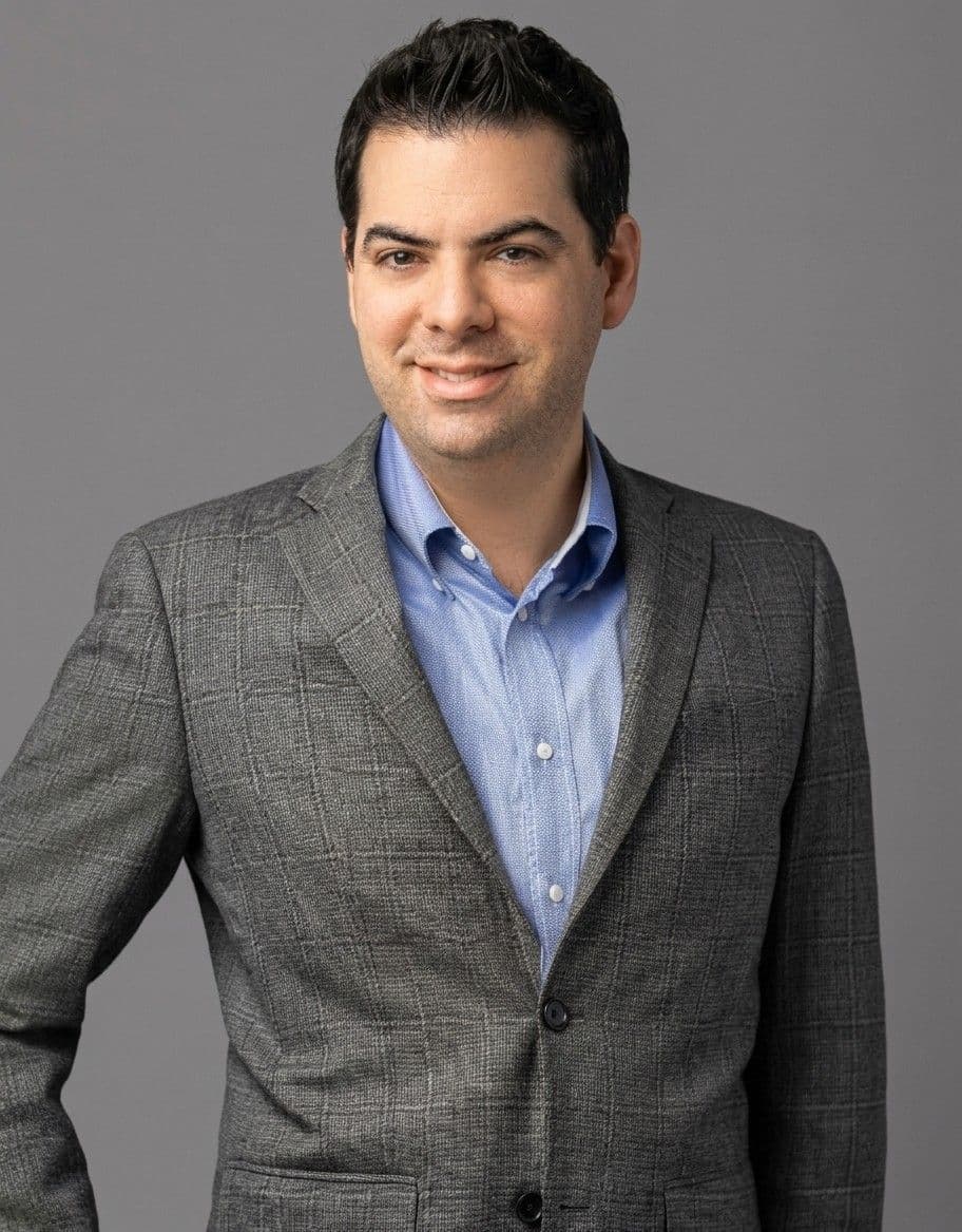 Portrait of a man wearing a gray blazer over a blue shirt.
