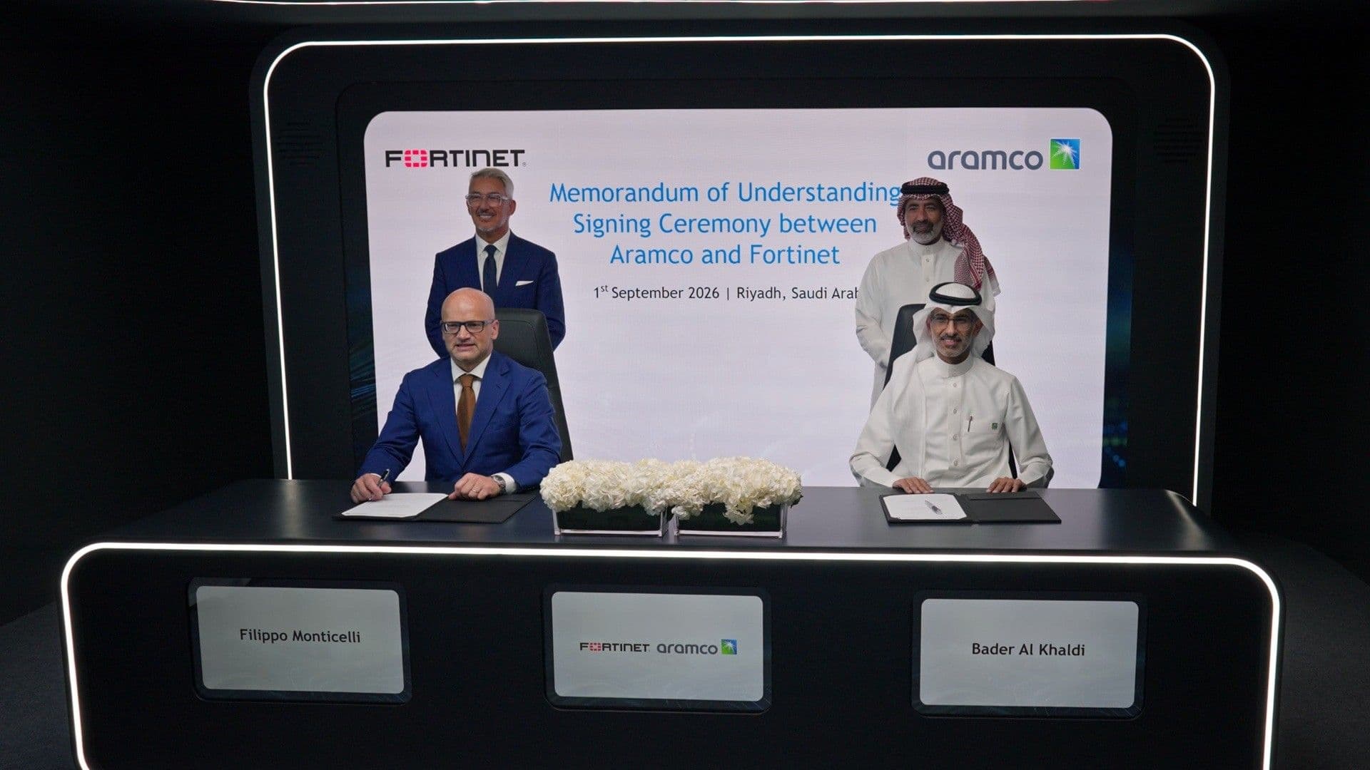 Representatives signing an agreement in front of Fortinet and Aramco branding.