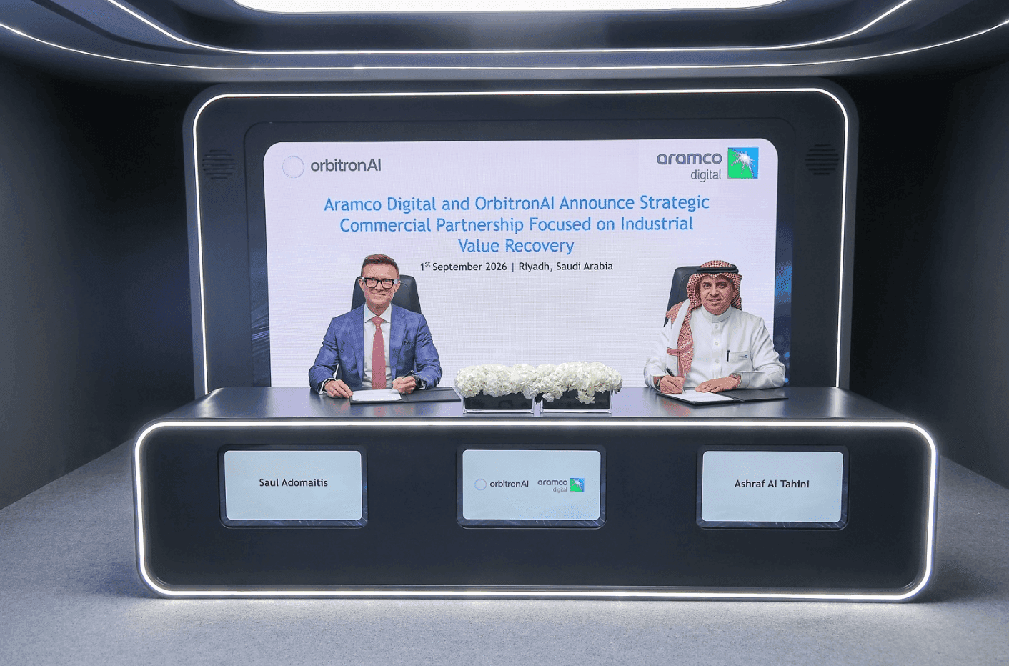 Two representatives signing an agreement in a display bearing Aramco branding.