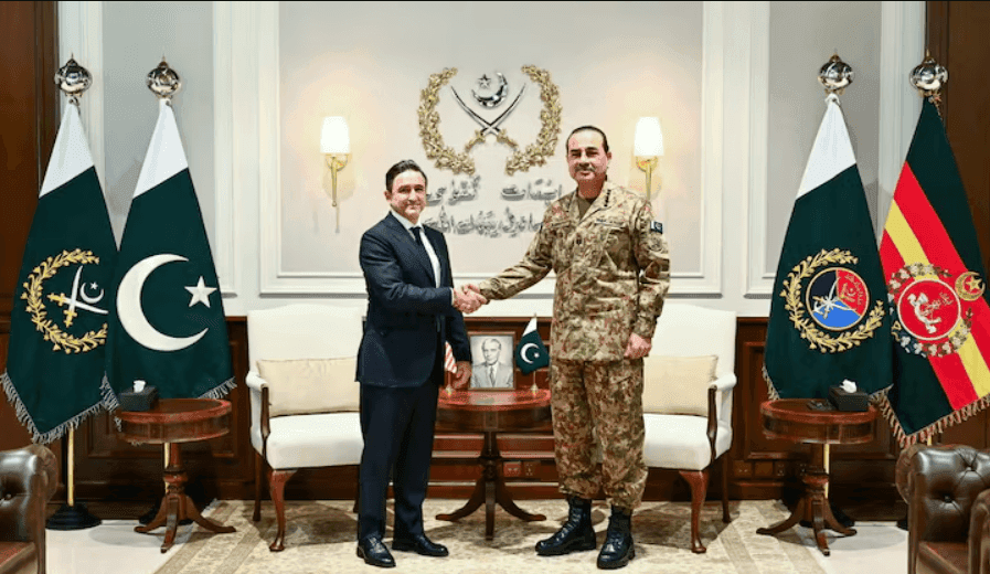 Civilian and military representatives posing with a document between national flags.