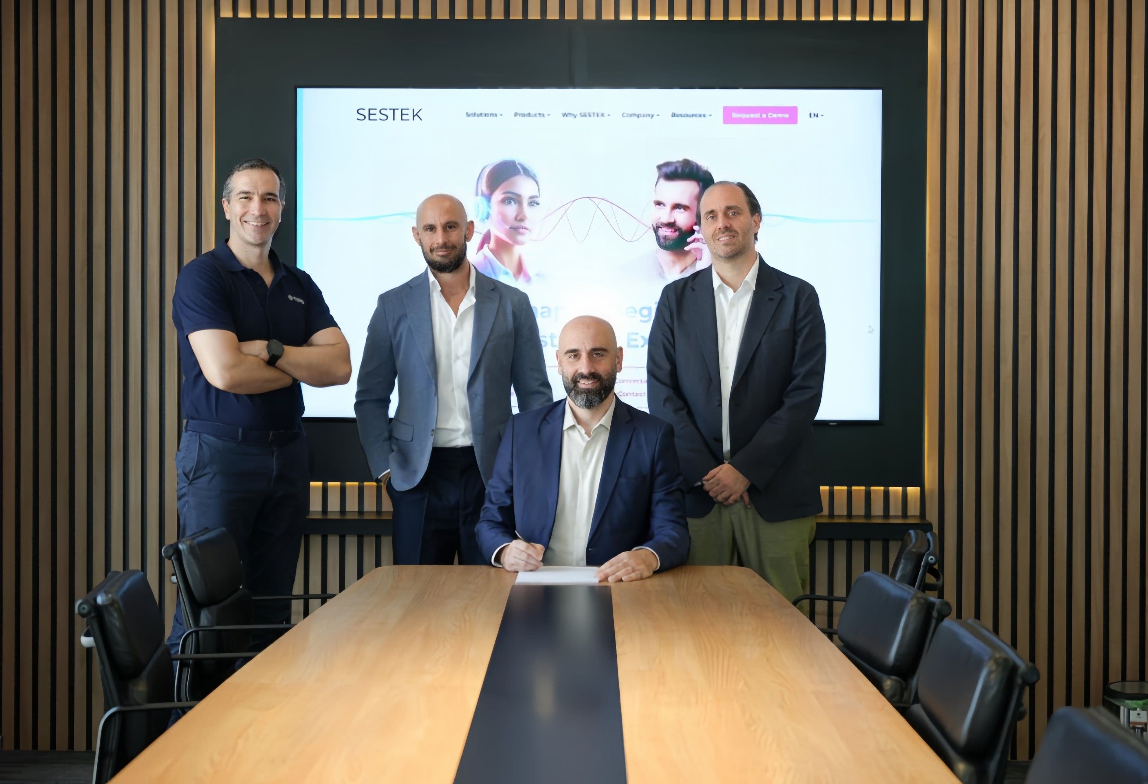 Four men posing beside a table holding a signed agreement.