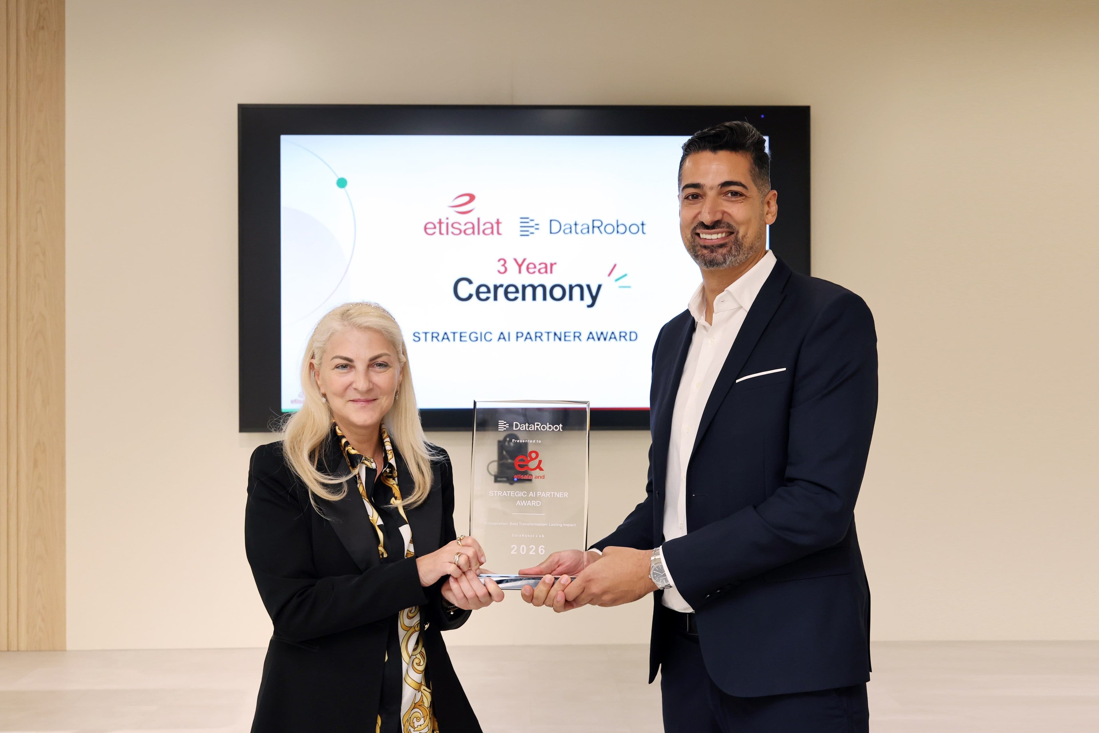 Two representatives holding an award in front of an event screen.