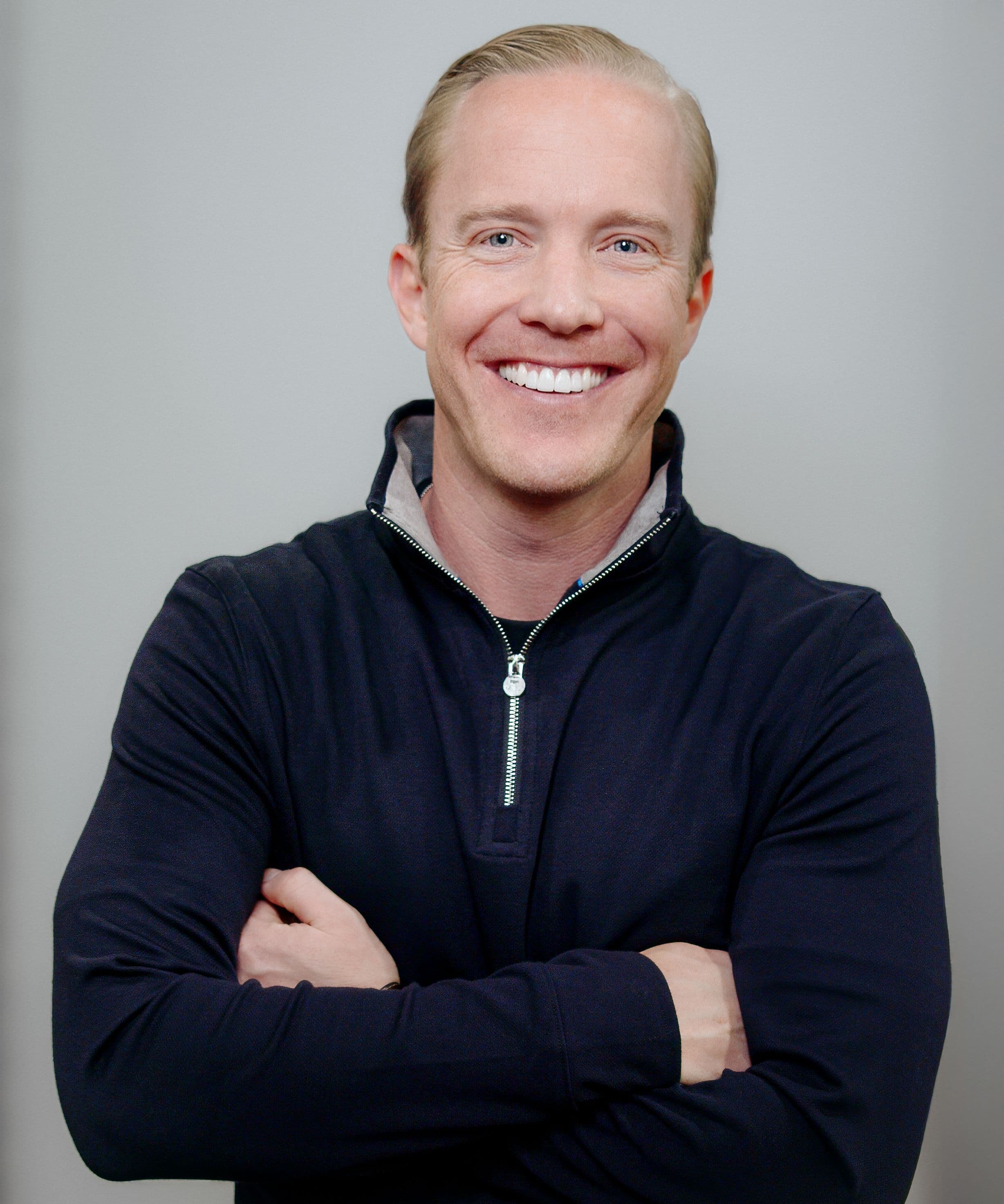 Portrait of a smiling man wearing a dark zip-neck top with his arms crossed.