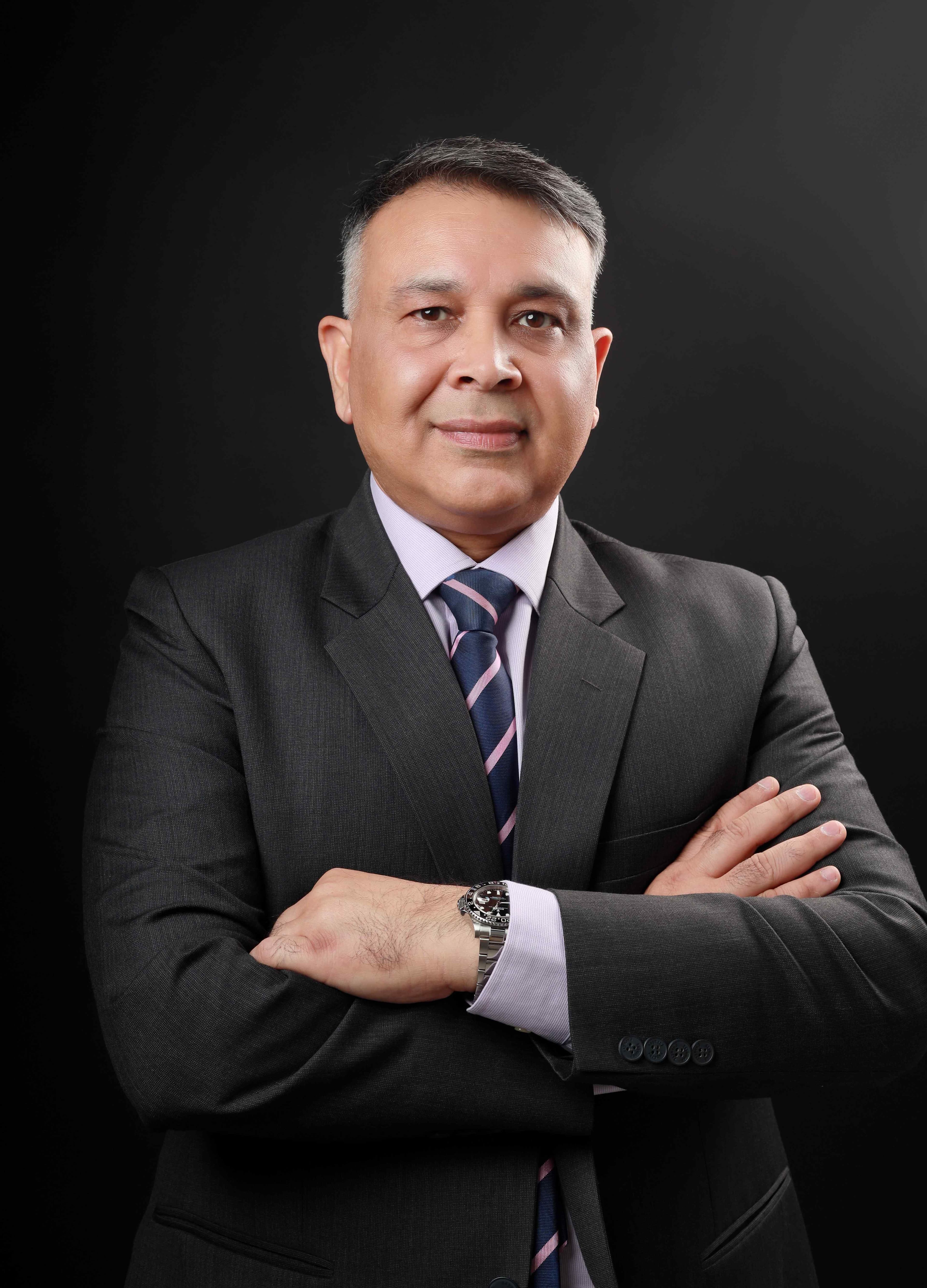 Portrait of a seated man wearing a dark suit and patterned tie with his arms crossed.
