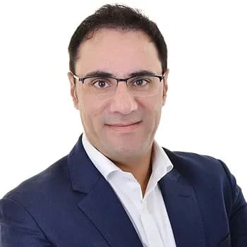 Portrait of a man wearing glasses and a dark jacket over a white shirt.