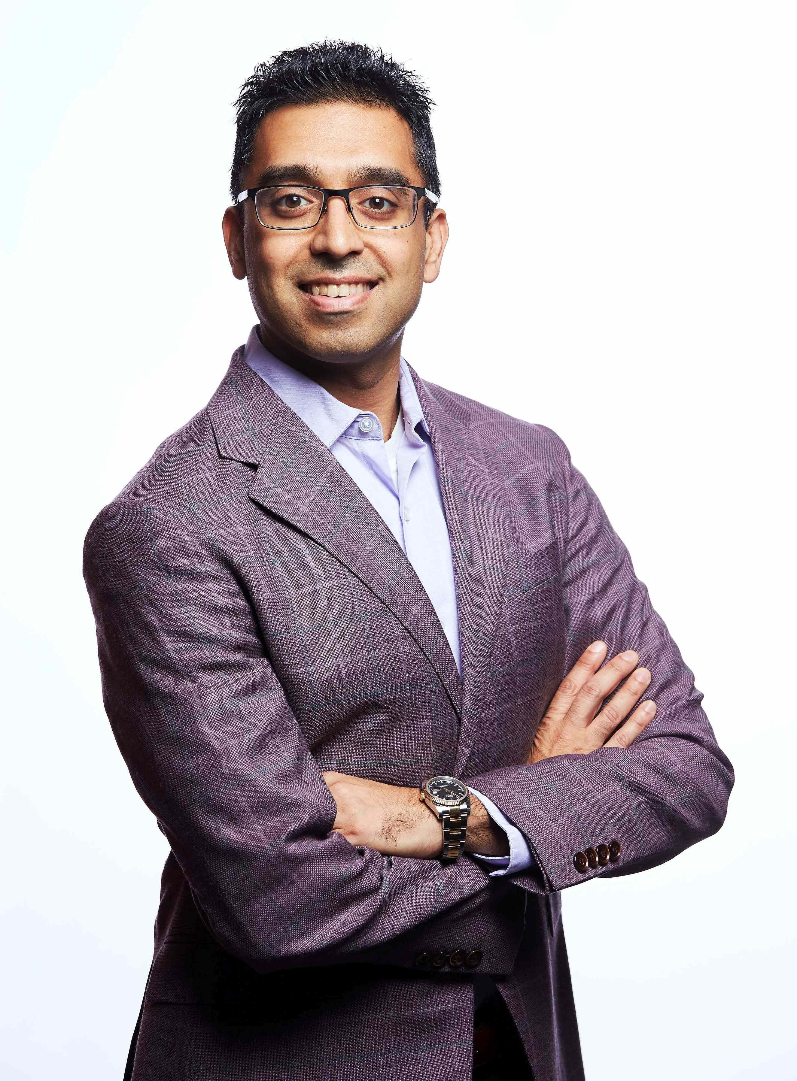 Portrait of a smiling man wearing glasses and a dark blazer with his arms crossed.