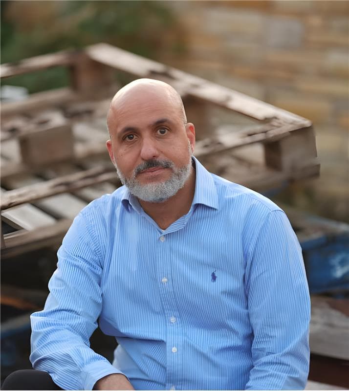 Portrait of a seated man with a gray beard wearing a light blue shirt.