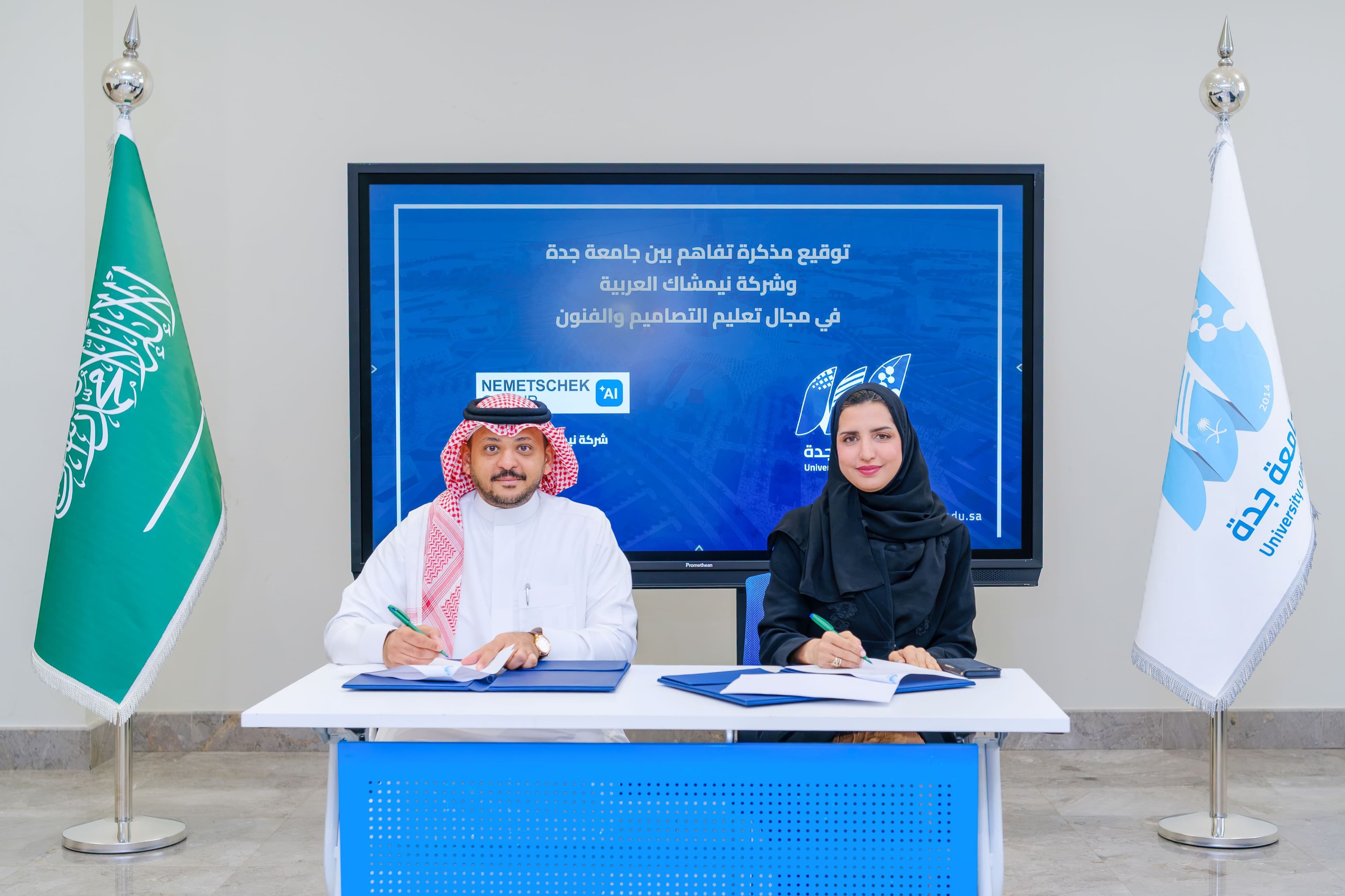 Two representatives seated at an agreement signing with a Saudi flag and organization banners.
