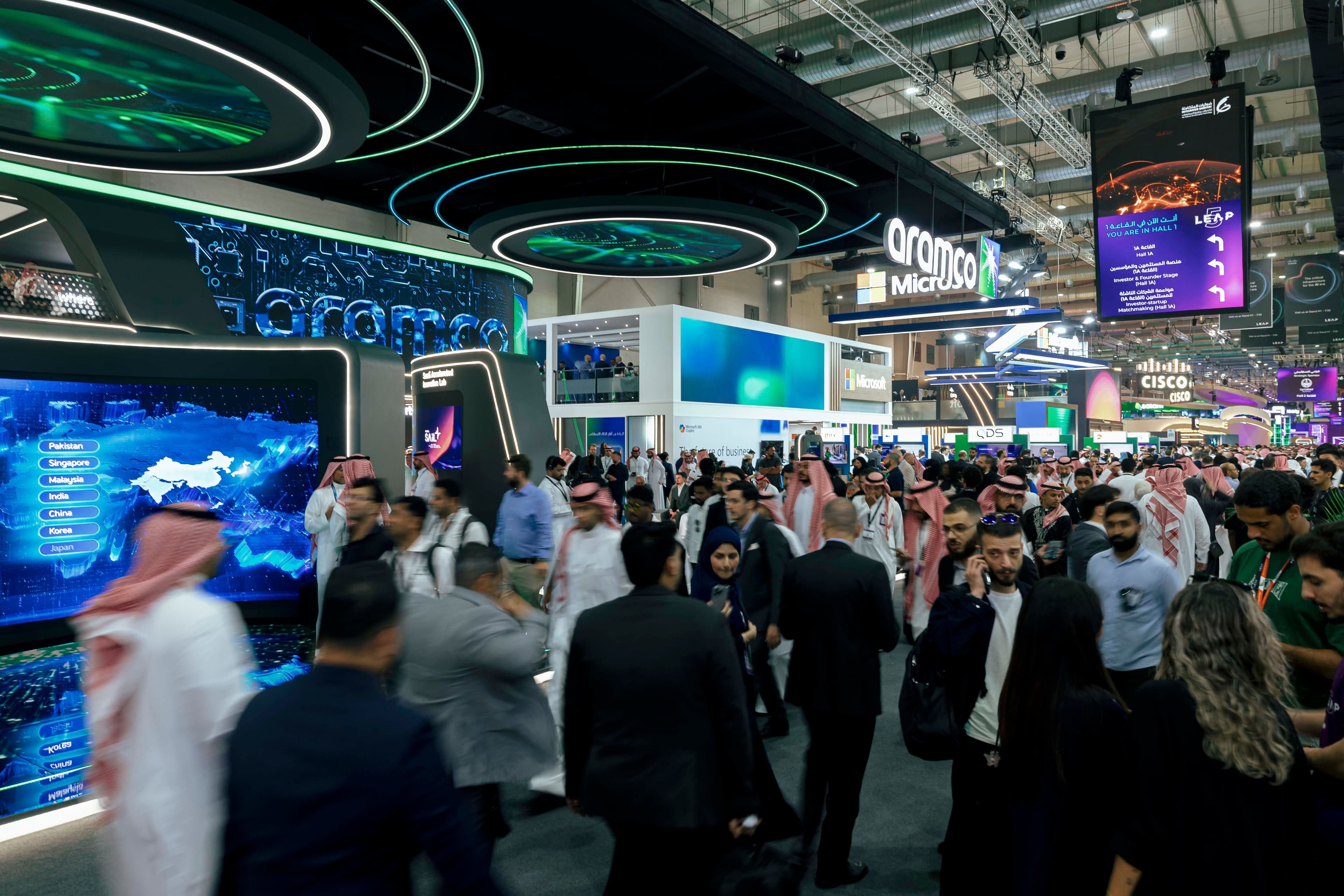 Crowded technology exhibition hall with illuminated overhead displays.
